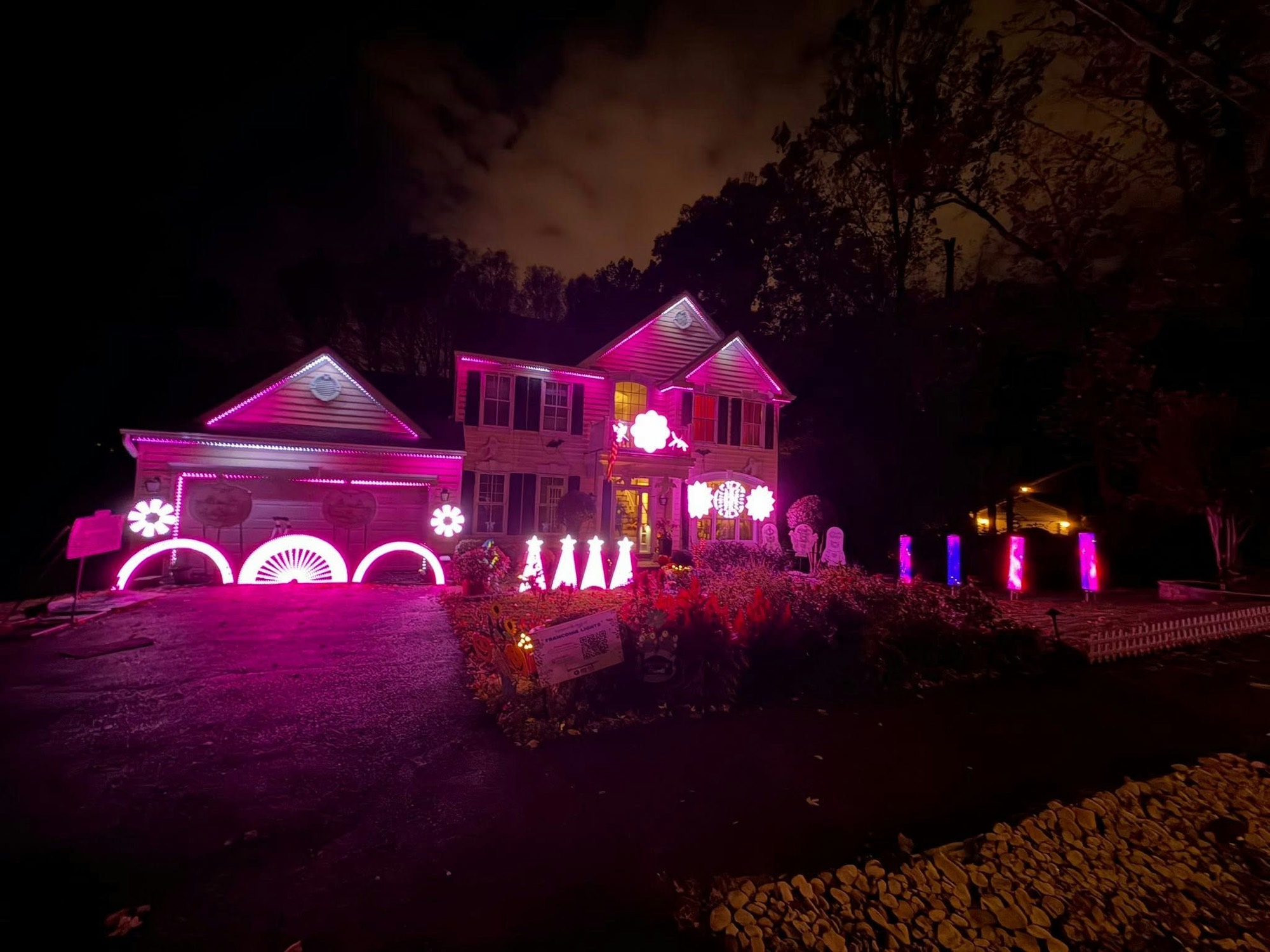 The Franconia Lights house at night, roofline and yard props glowing magenta during the Halloween show